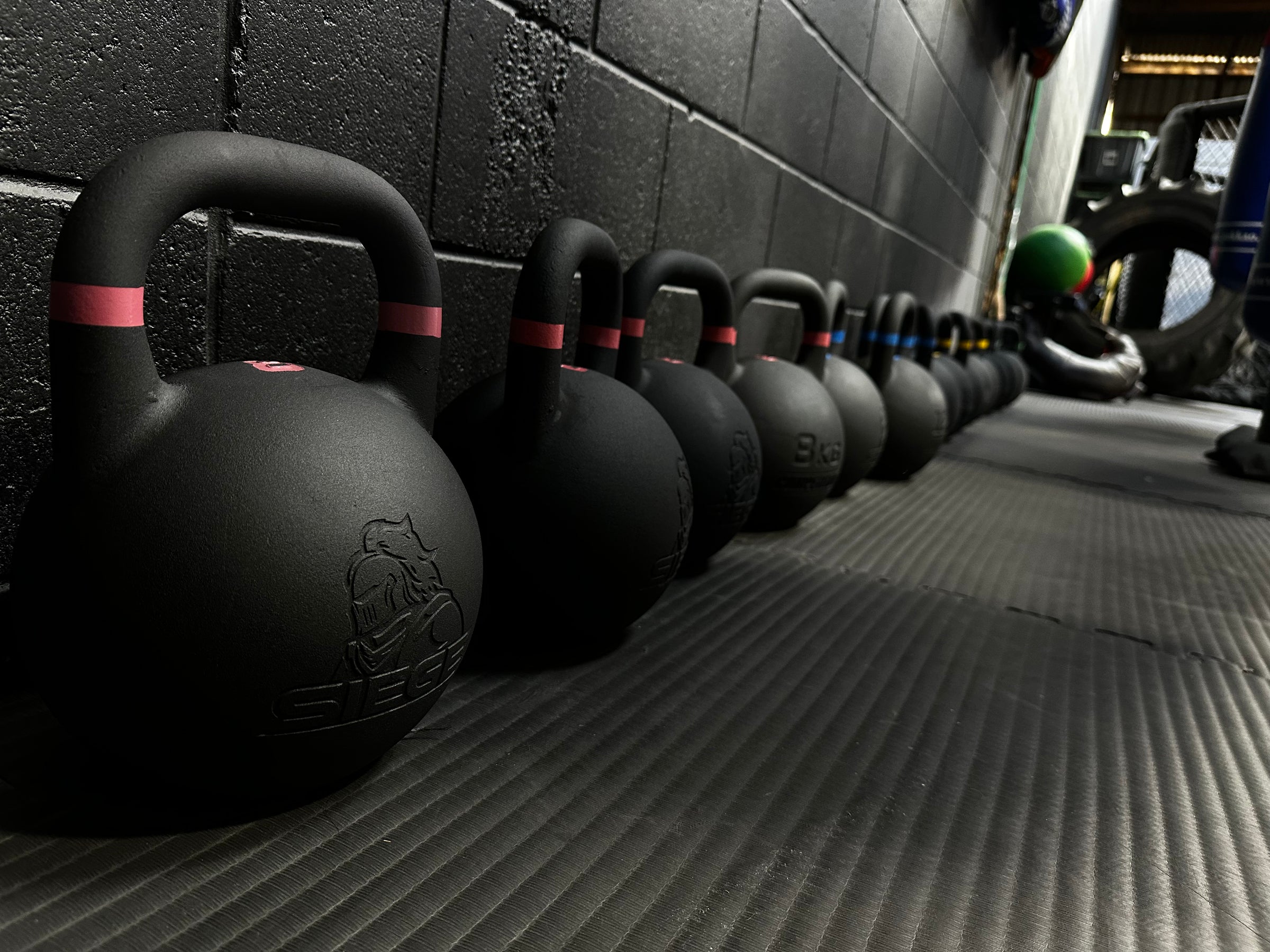 SIEGE matte black powder coat cast iron competition kettlebell gym fitout group photo along black gym wall